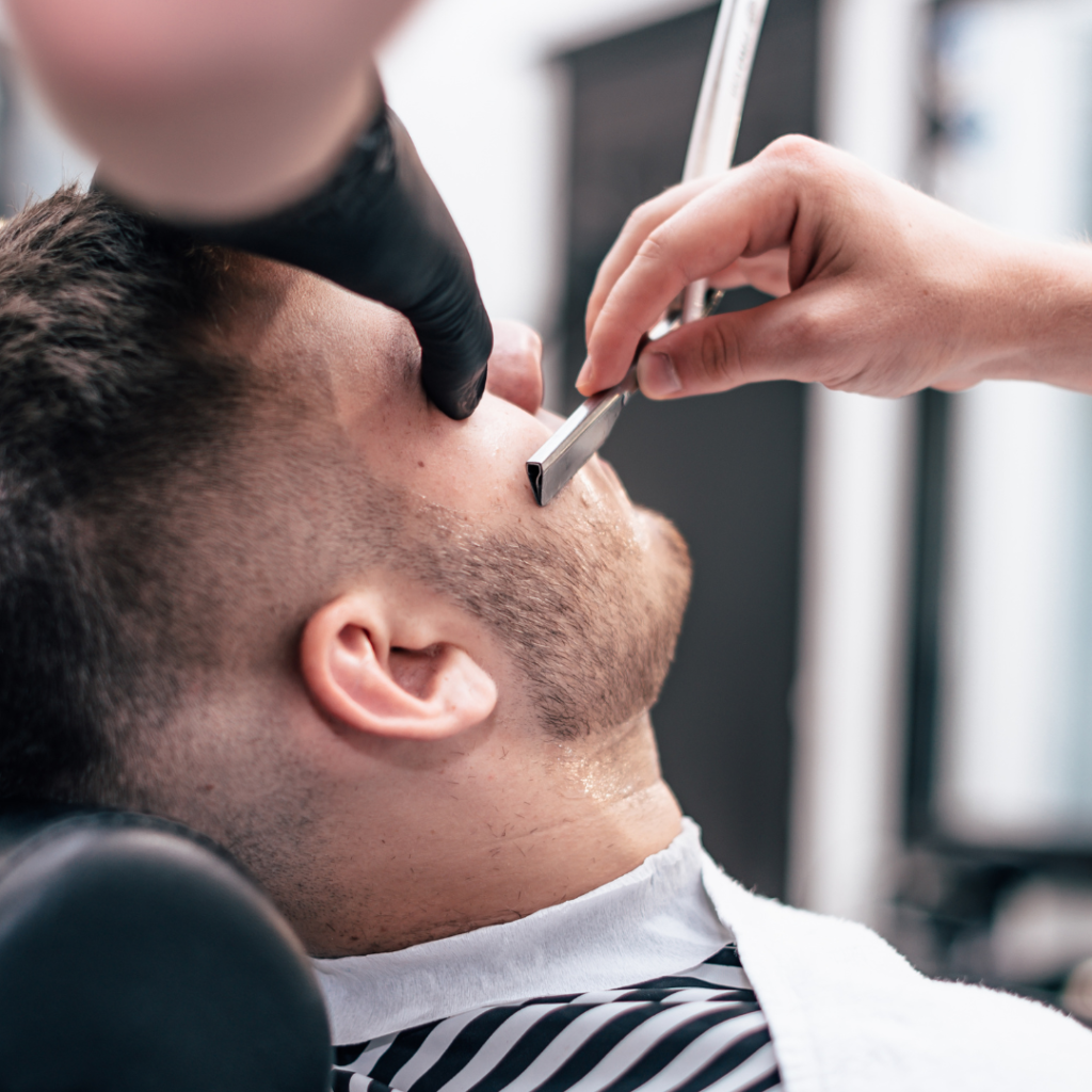 Barber shaving client's beard in barbershop.